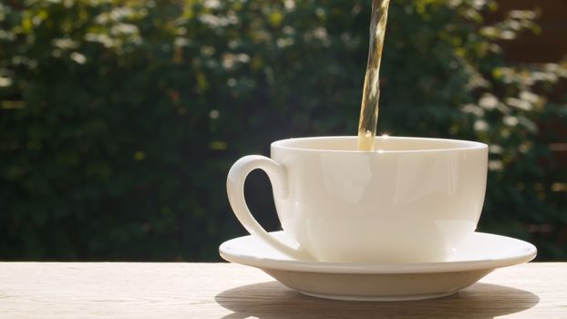 Close up hot tea pouring into a cup in the garden at summer day. Macro shooting