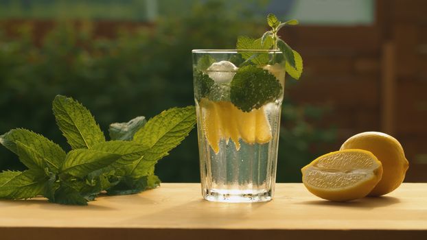 Close up tonic soda sparkling water with lemon, mint and ice in a glass on the table in the garden. Refreshing soft drink. Summer still life