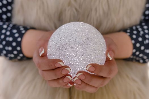 Close-up selective focus photography. Women's hands with a glittering christmas decoration. Christmas ball.