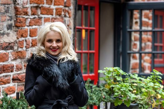 New, smiling, blond woman's portrait on the defocused red brick building in the background - image