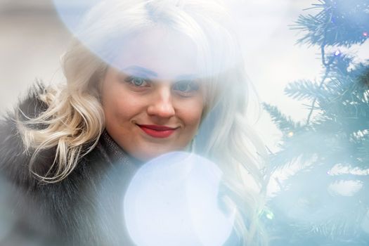 Portrait of a young smiling blonde woman photographed through the Christmas lights, soft focus - image