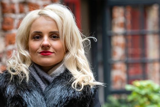 New, smiling, blond woman's portrait on the defocused red brick building in the background - image