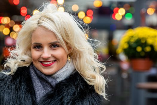 Portrait of a young smiling blonde woman against the background of defocused holiday lights. The concept of Christmas time. Copy space - image