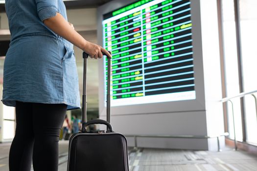 Woman with luggage wait and look at terminal gate information board checking for her flight in international airport. Suitcases in the departure lounge, holiday vacation concept, traveler suitcases