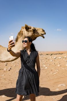 Woman taking selfie with a camel in the desert during a safari