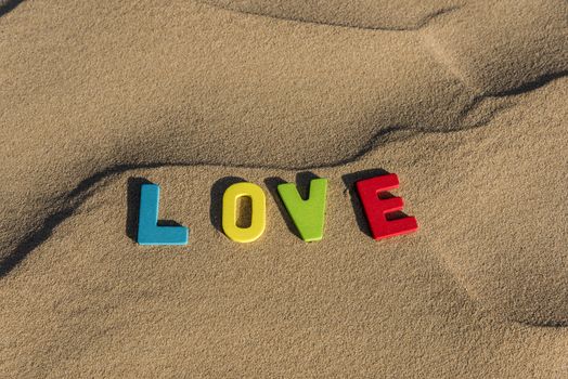LOVE word written with colorful letters on soft sand of the desert
