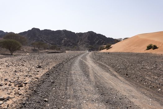 A 4x4 vehicle on a track in Wadi Al Ghail with the mountains and a dunes in the right side, Ras al Khaimah Emirates, United Arab emirates