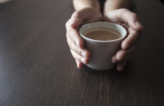 Hands hold a hot cup of coffee on a table