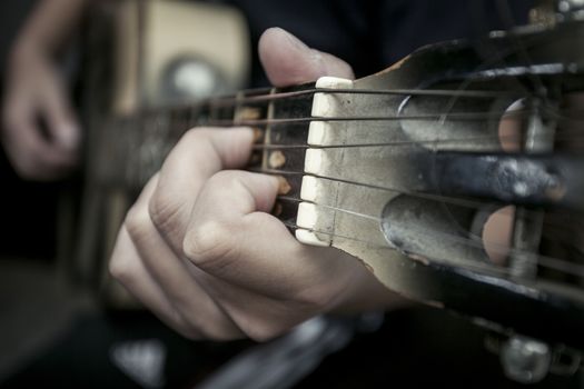 The man's hand close up holds a chord on a guitar signature stamp