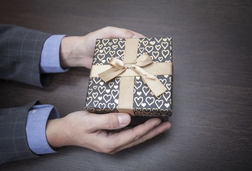 Man's hands keep a box in a business suit wrapped up by a bow