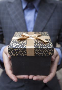 Man's hands keep a box in a business suit wrapped up by a bow