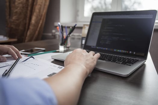 Man's hands make entries in the notebook, an open laptop in the face of