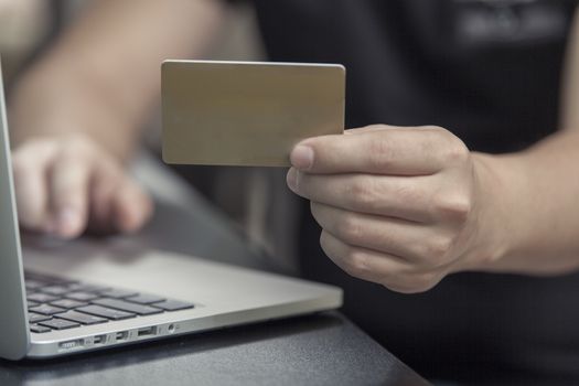 The man with a plastic card sits at the laptop and makes purchase online