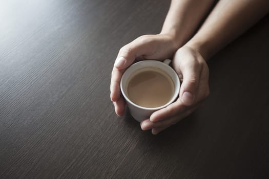 Hands hold a hot cup of coffee on a table