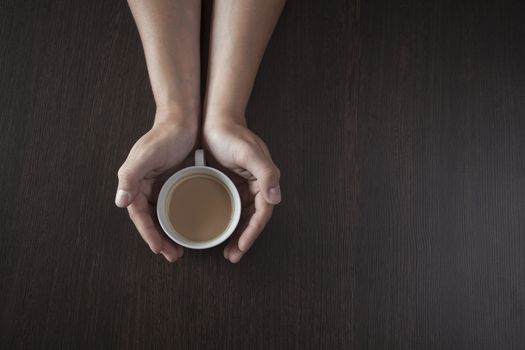 Hands hold a hot cup of coffee on a table