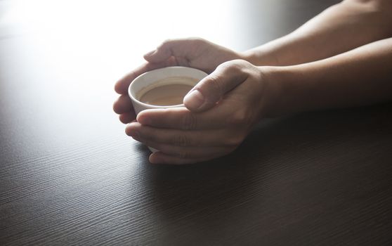 Hands hold a hot cup of coffee on a table