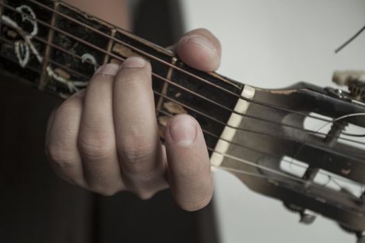 The man's hand close up holds a chord on a guitar signature stamp