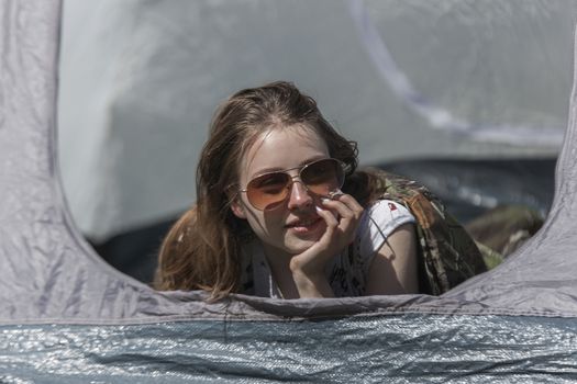 The girl looks out of tent and has a rest