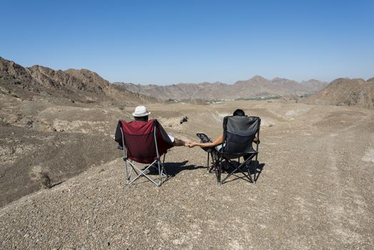 Couple in camping chairs over-looking a Wadi, mountains, in The United Arab Emirates