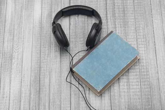 The book, big earphones lie on a wooden background, audiobooks