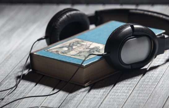 The book, big earphones lie on a wooden background, audiobooks