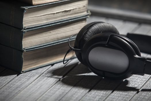 The book, big earphones lie on a wooden background, audiobooks