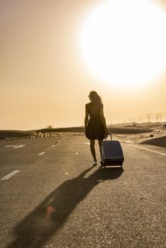 Woman walking with luggage on rural road in the desert with a car coming in the oposite side