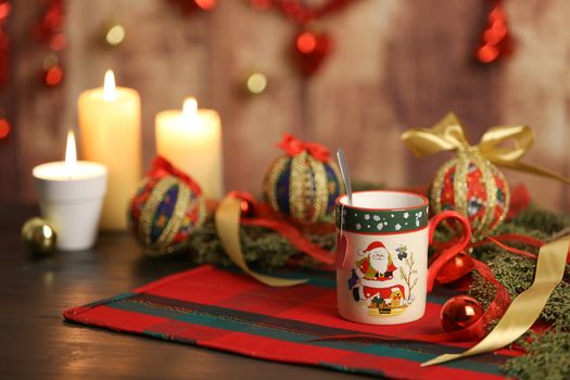 Christmas mug with empty tea label on Christmas table cloth with around pine branches, decoupage baubles, with lit candles and hanging Christmas decoration on wooden background with bokeh effect