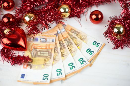 Christmas money business concept: some fifty euro banknotes with red and gold baubles and wreath decoration on light wooden table