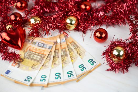 Christmas money business concept: some fifty euro banknotes with red and gold baubles and wreath decoration on light wooden table