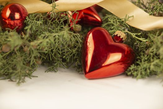 Close up of a Christmas red baubles with earth shape with around pine branches, red baubles and satin gold ribbon on wooden background with bokeh effect