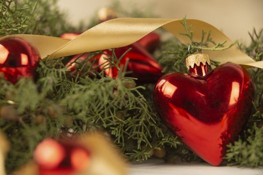 Close up of a Christmas red baubles with earth shape with around pine branches, red baubles and satin gold ribbon on wooden background with bokeh effect