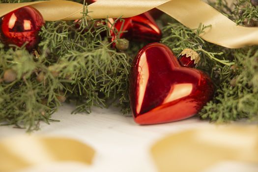 Close up of a Christmas red baubles with earth shape with around pine branches, red baubles and satin gold ribbon on wooden background with bokeh effect