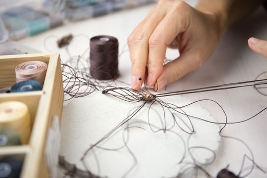 Lifestyle concept, work from home to reinvent your life: close-up detail of woman hands making macrame knotted jewel with some colored thread spools in foreground and bokeh effect