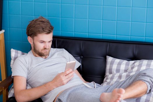 Happy man watching media content in a smart phone sitting on a couch at home.