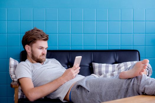 Happy man watching media content in a smart phone sitting on a couch at home.