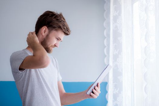 bearded man using tablet while standing near the window in his modern apartment.Concept young business people working at home.