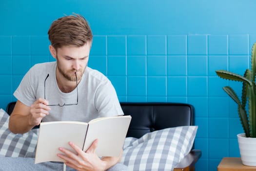 Young man reading book on sofa in the living room.