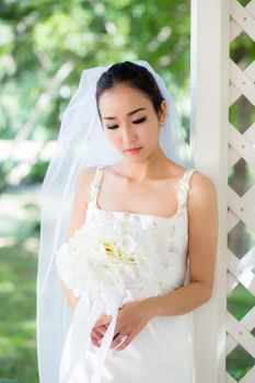 bride in a dress standing in a green garden and holding a wedding bouquet of flower.
