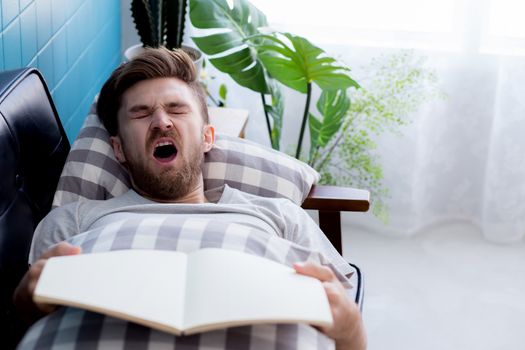 Man reading book with yawn sleep in couch sofa.