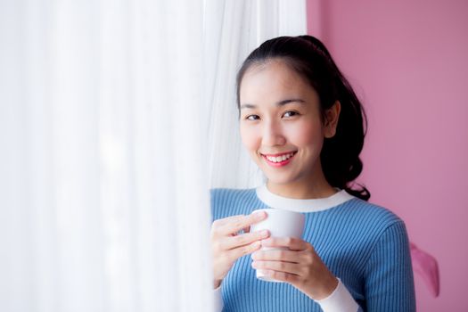 Beautiful young woman is looking out the window and holding a cup of coffee in morning.