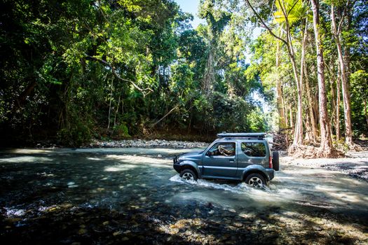 A car drives along Cape Tribulation Rd and crosses a river near Cape Tribulation in the Daintree, Queensland, Australia