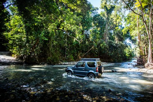 A car drives along Cape Tribulation Rd and crosses a river near Cape Tribulation in the Daintree, Queensland, Australia