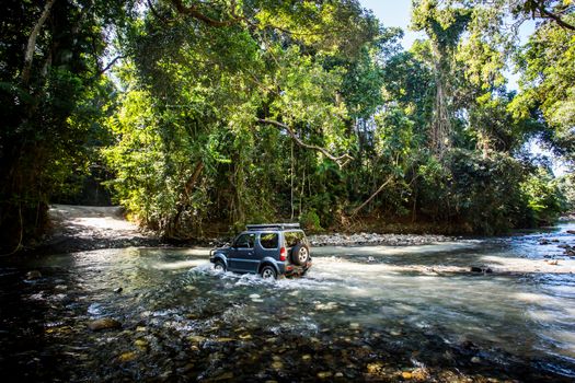 A car drives along Cape Tribulation Rd and crosses a river near Cape Tribulation in the Daintree, Queensland, Australia