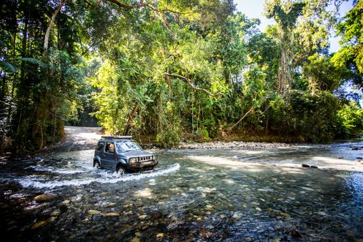 A car drives along Cape Tribulation Rd and crosses a river near Cape Tribulation in the Daintree, Queensland, Australia