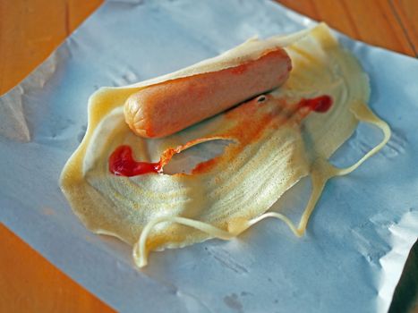 Hot Dog wrapped in bread topped with sauce on a paper-based floor and a wooden table.
Junk food concept.