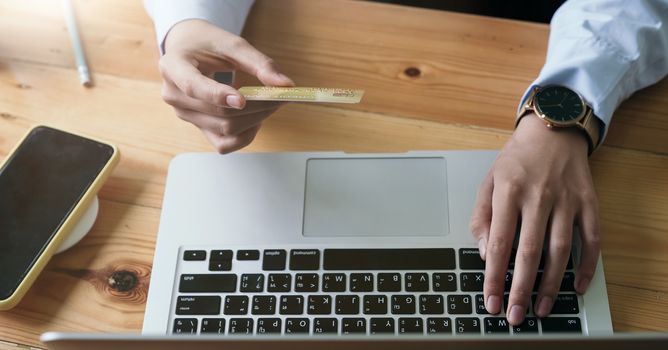 Close up hand of woman holding credit card and using laptop computer at home. Online shopping concept.