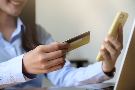 Close up hand of woman holding credit card and using laptop computer at home. Online shopping concept.