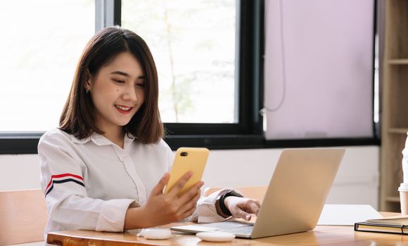 Asian girl works from home or a student is studying from home or a freelancer. She uses a smart phone and laptop computer.