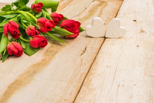 Bunch of red tulip flowers with two hearts on wooden background with copy space